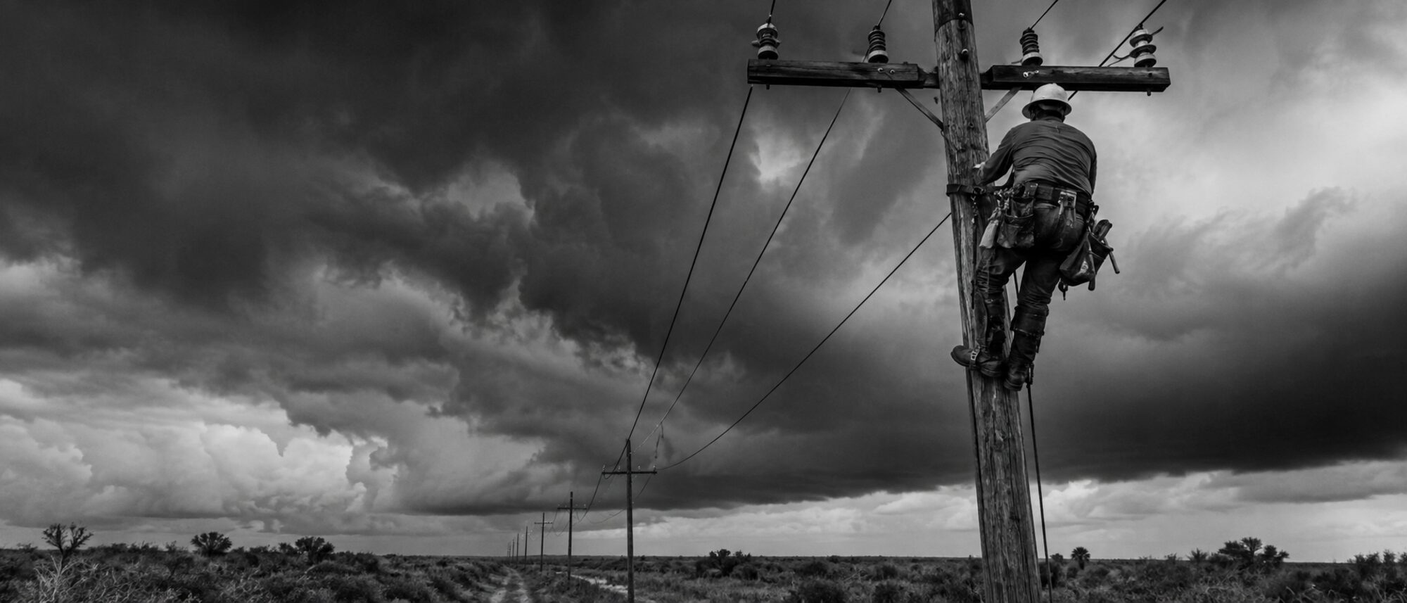 A lineman climbing a utility pole under a storm sky